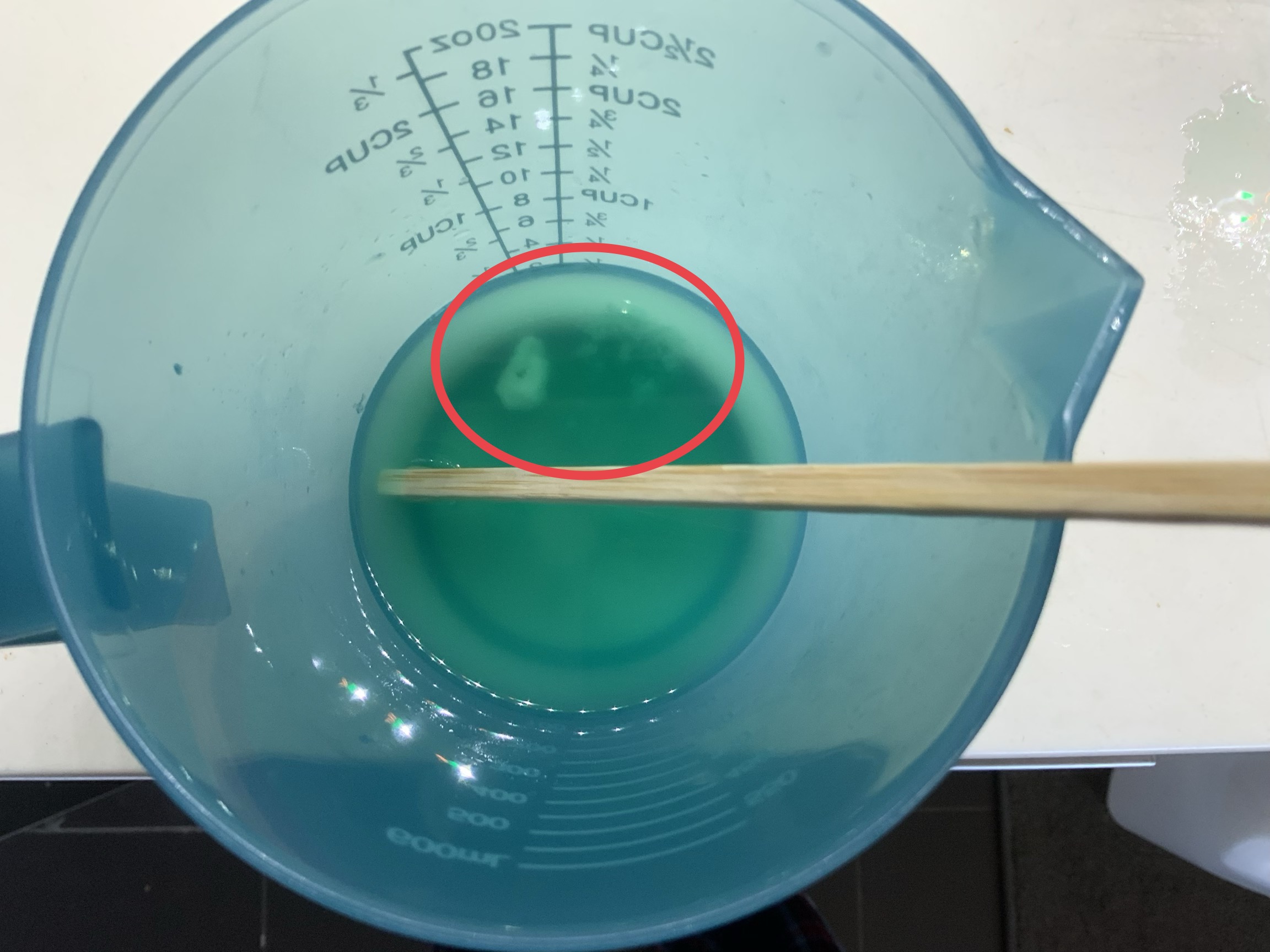 container holding greenish solution with white substance visible at the bottom