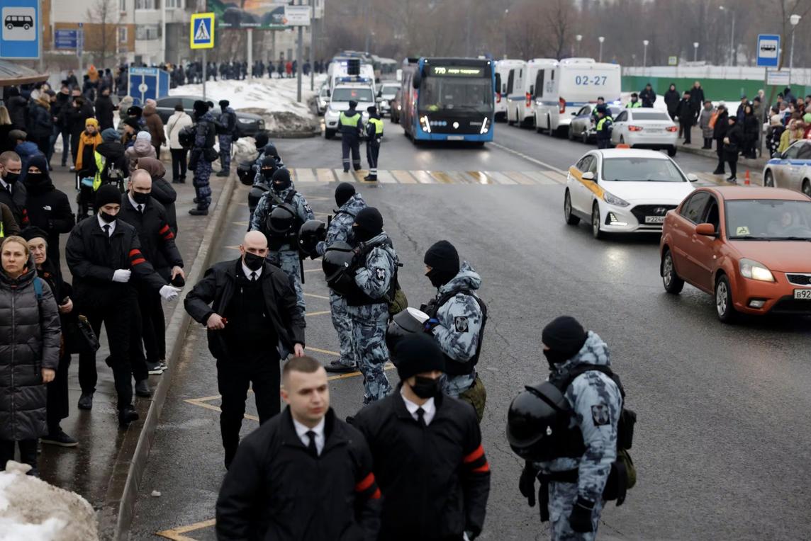 Several Russian peoples along the side of a street; some men are wearing red and black armbands