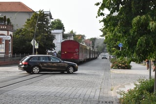 Molli running on the road with a car passing by on the wrong side because it needs to pass the train.