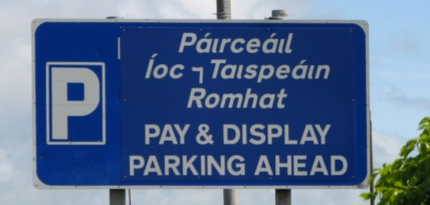 Sign saying "Páırceáıl Íoc ⁊ Taıspeáın Romhat — PAY & DISPLAY PARKING AHEAD"