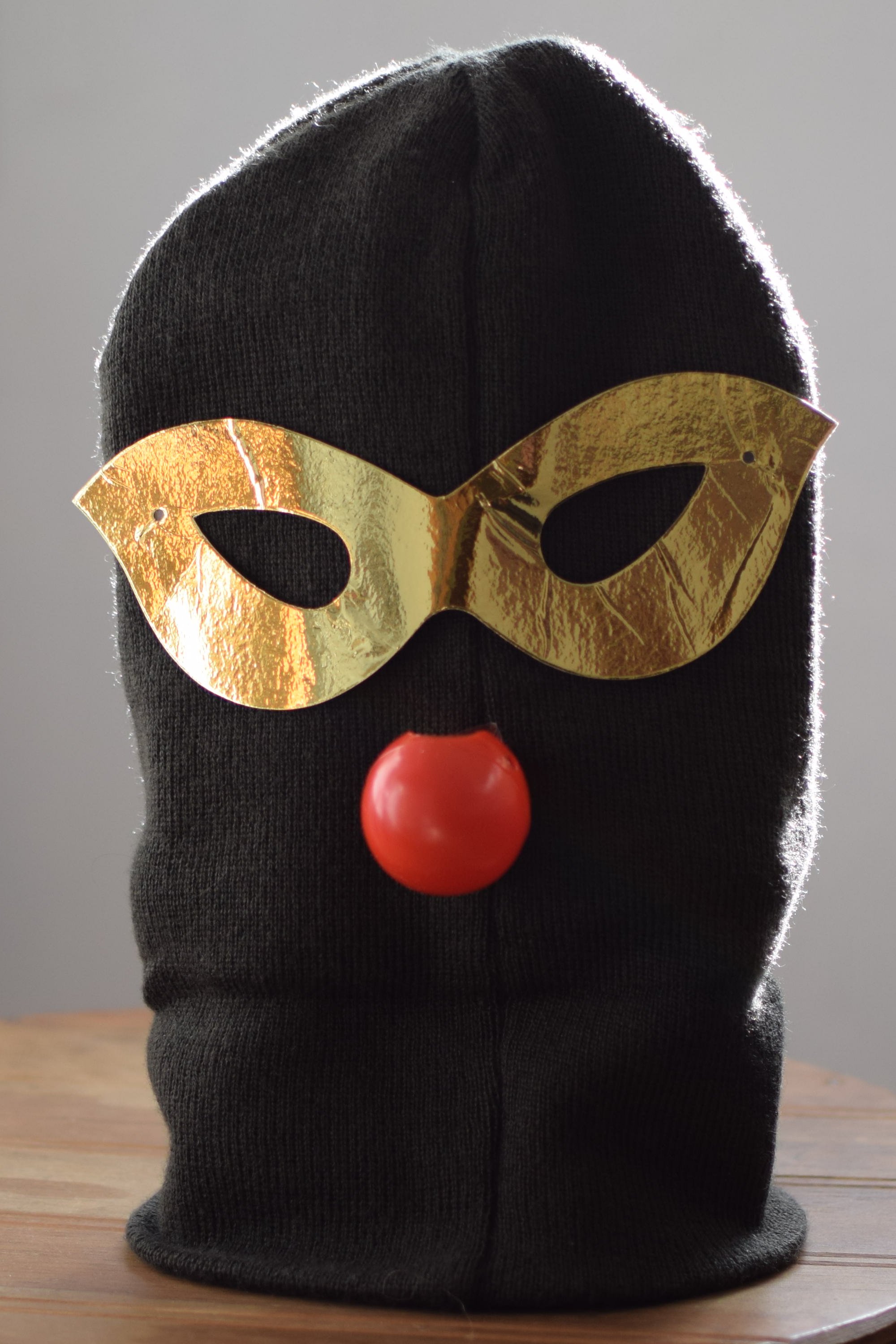 A green/grey beany with golden Venetian-style eye mask and red nose