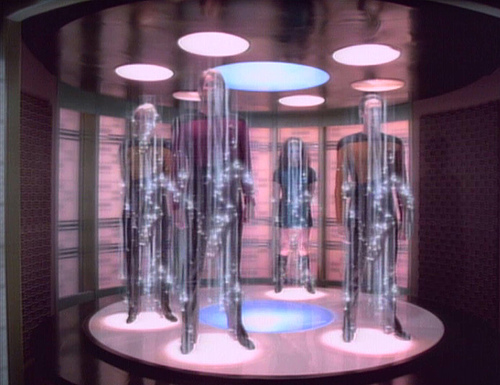 Yar, Riker, Troi and Data are being transported.  The effect shows them surrounded by irregular clusters of points of white light, mostly around their midsection, with white rays extending vertically up and down to mostly envelope a cylindrical space surrounding each.