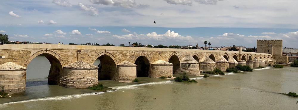 Roman bridge of Córdoba in real life, a long spanning bridge with multiple arches leading into a gatehouse