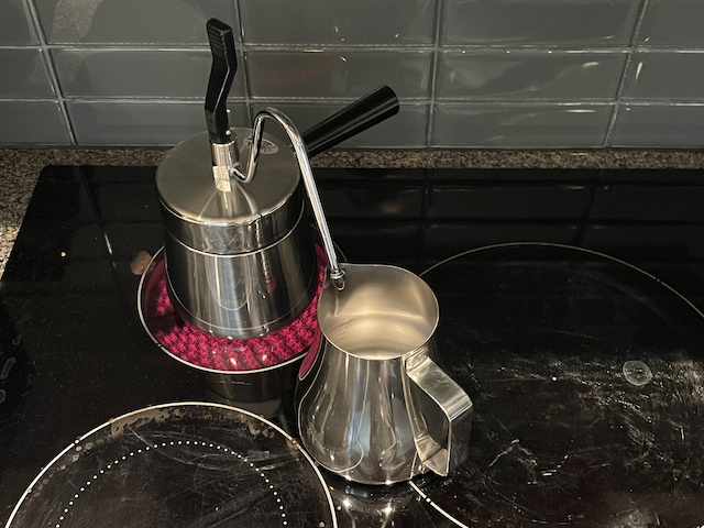 A stovetop coffee maker on a stove, with a pitcher ready to catch the brewed coffee