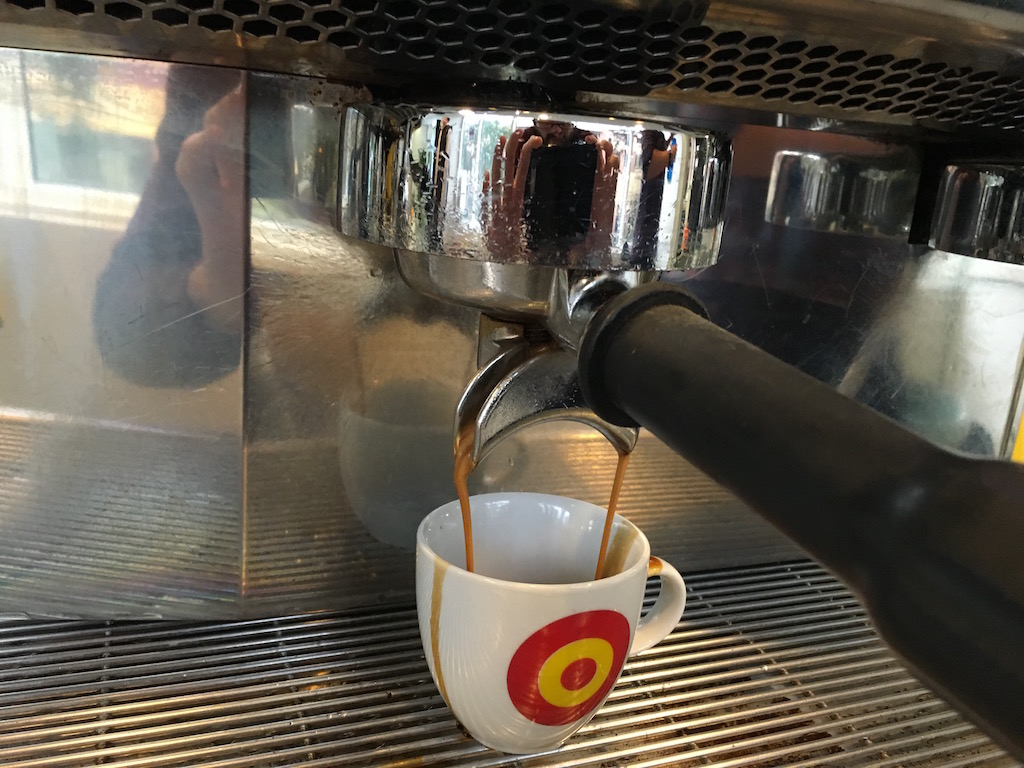 Photo of a demitasse underneath a double espresso handle, with a streak of coffee down the outside.