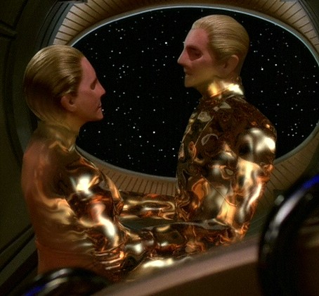 Odo and female founder linking, their heads in their stereotypical changeling humanoid form while their bodies are turning into liquid