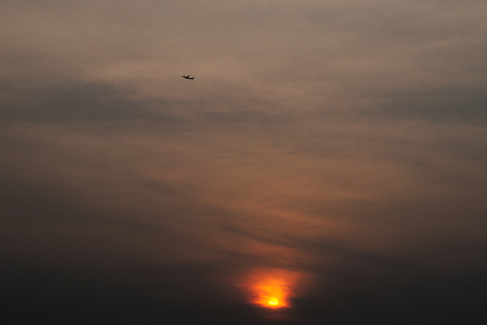 A fiery sun rising, with a plane rising above