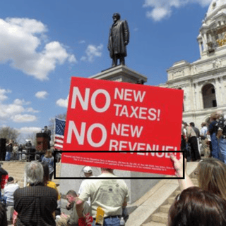 picketer holding a sign with large printed message with small printed text at the bottom.