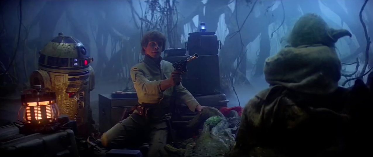 Luke, R2 and Yoda sit in the makeshift camp in the Dagobah swamps; Luke raises his blaster at the potential threat of Yoda