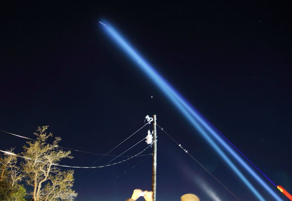 image of laser and spotlights being pointed at the ISS from Earth