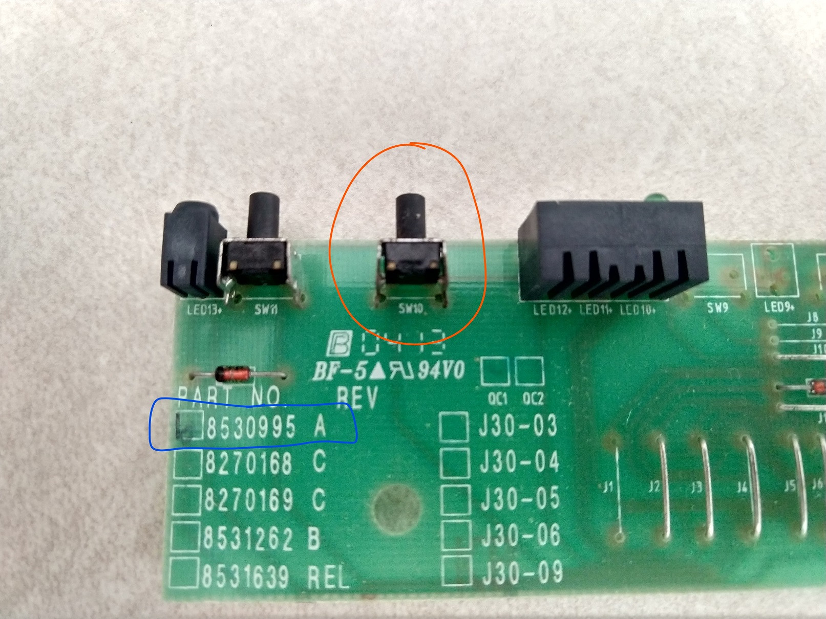 Control board from front with faulty switch circled in orange and board model number circled in blue